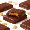 Barritas Cuadrito Fitkery bañadas en chocolate con maní sobre fondo blanco